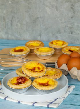 tatlı yumurtalı tart veya Portekiz yumurtalı tart tatlı krema beyaz tabak ve mavi ahşap masa içinde yumurta malzemeleri