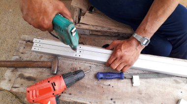 Adam alüminyum çerçevede sondaj yapıyor ve atölyenin üst görünümünde ev dekorasyonu yapıyor.