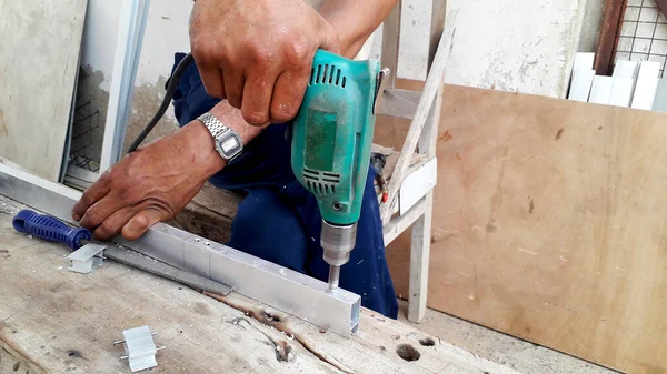 Adam alüminyum çerçevede sondaj yapıyor ve atölyede ev dekorasyonu yapıyor.