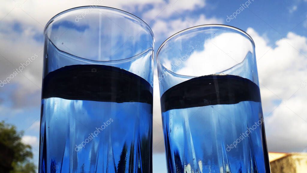 two water filled blue glasses with unique perspective and cloudy sky in background