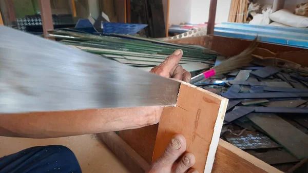 Marangoz levhayı demir testeresiyle elle kesiyor.