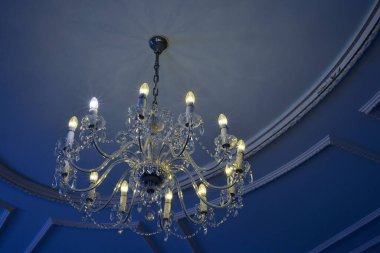 Mavi tavanın altındaki cam bir avizede enerji tasarrufu ile normal ampullerin karşılaştırılması.