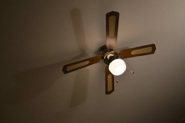 Mediterranean brown wood and material ceiling fan casts a long shadow on a plaster ceiling.