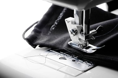 Tamamen siyah bir yüz kaplaması dikiş makinesine dikilmiş. Sol tarafta boş beyaz kopyalama alanı. Karşıt resim.