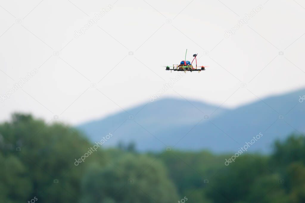 Small home made FPV racing quad copter camera drone flies in front of the malvern hills and trees. Selective focus on this autonomous aircraft