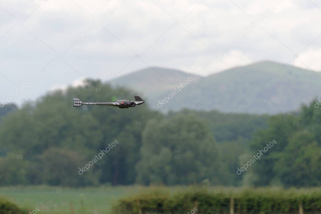 Flying low and fast in front of the malvern hills, a remote control FPV first person view flying wing is in selective focus. Propeller blurred.