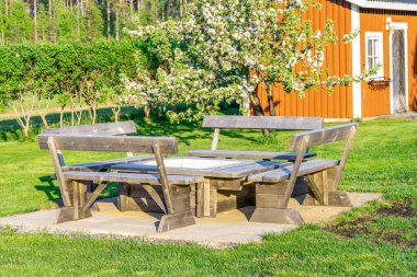 Yeşil İsveç bahçesinin ortasında, yaz ortasında beton tabaklarda duran masa ve bankları olan şık ahşap barbekü mekanı. Vasterbotten, Kuzey İsveç, Umea