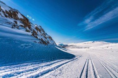 Kuzey İsveç, Lappland 'deki Atoklinten Dağı' nın sonundaki yan manzara. Bütün kar araçları buraya gelir, bir sürü patika vardır. Parlak güneş tepede parlıyor, kar, mavi gökyüzü, çokça kopyalama alanı.