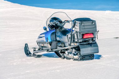 Bir mavi kar aracı Norveç dağlarının yamacında, kıtır bir karın üzerinde duruyor. Sıcak bir gün ve çok parlak bir güneş, bulutlar yok, dağlar kış manzarası. Emniyet kaskı ön camın altında