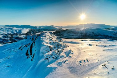 Norveç 'in karlı kış dağları üzerinde, huş ağaçları ve çam ağaçları ile günbatımı altın ışık, sakin mavi gökyüzü. Atoklinten dağ bölgesi, Joesjo, Lappland belediyesi, Kuzey İsveç