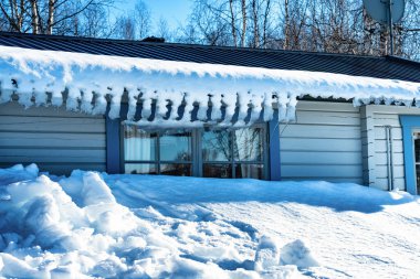 İsveç 'in kuzeyindeki Lappland Dağları' ndaki geleneksel açık mavi kulübenin çatısından sarkan kar ve eğri buz saçakları fotoğrafı..