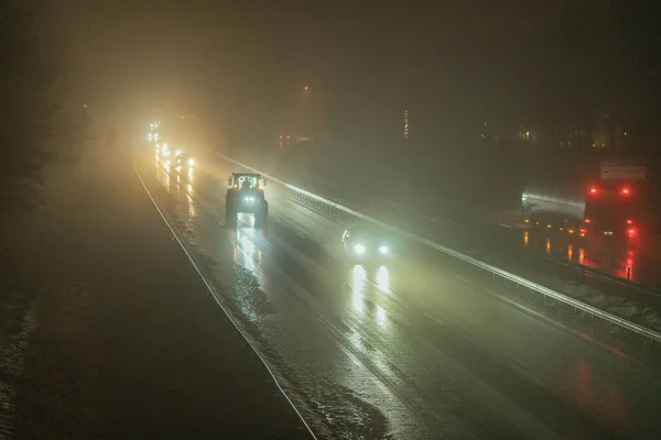 Many fast cars and slow tractor driving in both directions on motorway in heavy thick fog at late dark evening, warm autumn, European highway E4, outside of Umea city, Vasterbotten, Northern Sweden