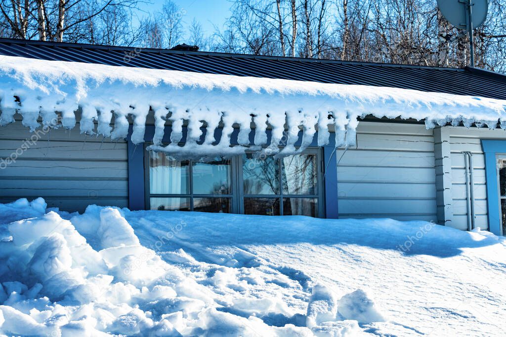 Photo of snow and bent icicles hanging from the roof of traditional swedish wooden light blue cabin in Lappland mountains, Northern Sweden.