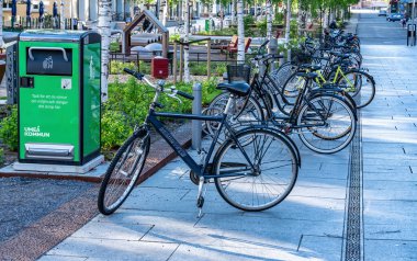 UMEA, SVEDEN - 10 Haziran 2020: Yeşil geri dönüşüm kutusunun yakınına park edilmiş bir sürü bisiklet ve çocuklar için küçük bir oyun parkı, Umea şehrinin merkezi bölümü, Vasterbotten. Güzel bir yaz günü.