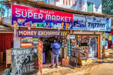 CALANGUTE, GOA, INDIA JANUARY 2, 2019: Sokak fotoğrafı: Para değiş tokuşu ofisi ve dövme stüdyosu aynı küçük evde, para değişimi için girişte duran bir adam. Goa 'da güneşli bir gün, güzel bir gün