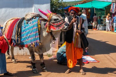 ANJUNA, GOA, İNDİYA HAZİRAN 2, 2019: Renkli bir boğaya yakın duruyor, müzik aletini tutuyor, dostça gülümsüyor ve başparmak işareti gösteriyor.