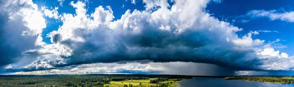 Aerial Panorama of Scandinavian pine tree forest landscape, Sunny and Rainy areas around lake, blue sky, white and dark clouds, green yellow fields. View on typical landscape of Northern Sweden