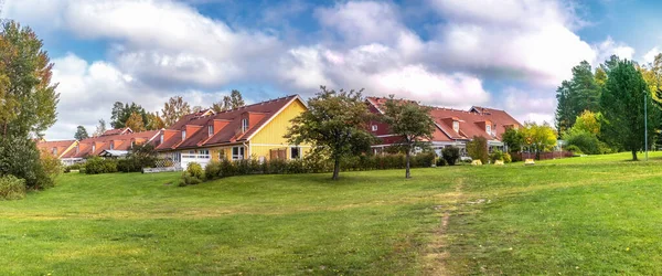 Typical Swedish middle class wooden terraced houses in Umea. Residential yellow townhouses with red orange clay tiles on blue sky with big white clouds background on sunny autumn day. Green grass.