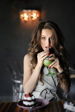 Güzel bir kızın dikey portresini kapat, günlük kıyafetlerini giy, restoranda ya da kafede otur, kokteyl iç. Pastalı kız.