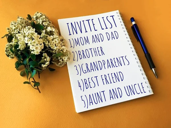 Invite list on a white Notepad for the wedding day.Notepad, Pen and flowers on a yellow background.The wedding fuss.Photos for the wedding.