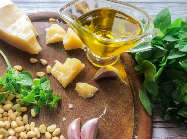 Pesto sosu yapmak için gerekenler: ön planda, bulanık arkaplanda sarımsak karanfilleri: yeşil fesleğen, parmesan peyniri, zeytin yağı, ahşap zeminde çam fıstığı. Seçici odak