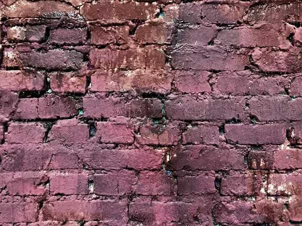 Old brick wall with several layers of old paint with streaks of different shades of pink, brown, purple, purple, interspersed with turquoise and blue