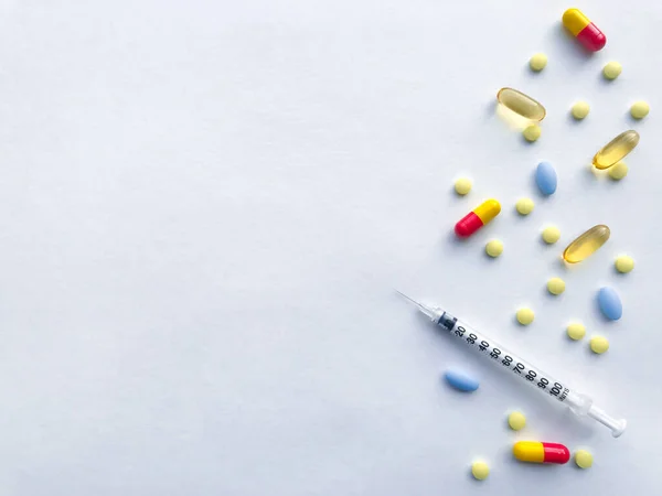 许多彩色药丸和胰岛素注射器在右边的白色纹理粗糙的纸片的背景上 有文字的地方 — 图库照片