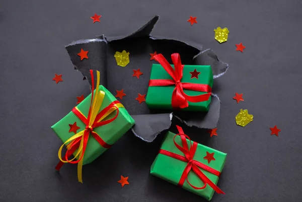 Gifts in green paper with red and yellow ribbons and confetti in the form of red stars and gold presents fall out a torn hole in the black paper. Big  sale concept