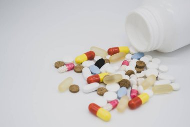 Beyaz arka planda beyaz bir şişeden çok renkli haplar düşüyor.