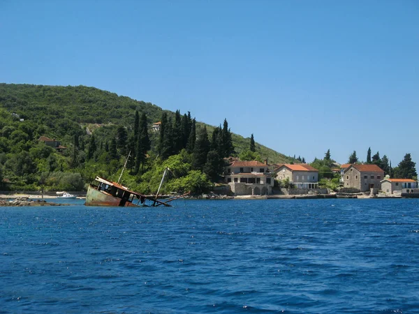 在明亮的蓝色大海中 在一座绿色山脚下的海滨房屋的衬托下 一艘沉船的残骸 — 图库照片