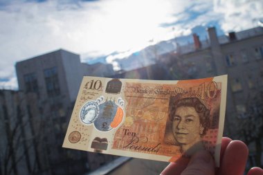El, Queen ve Jane Austen 'in portresiyle polimer plastikten yapılmış yepyeni bir 10 sterlin tutuyor. Ve bankadaki şeffaf bir pencereden yansıyor.