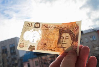 El, Queen ve Jane Austen 'in portresiyle polimer plastikten yapılmış yepyeni bir 10 sterlin tutuyor. Ve bankadaki şeffaf bir pencereden yansıyor.