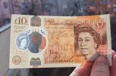 El, Queen ve Jane Austen 'in portresiyle polimer plastikten yapılmış yepyeni bir 10 sterlin tutuyor. Ve bankadaki şeffaf bir pencereden yansıyor.