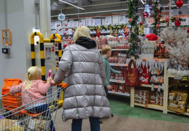 Moskova, Rusya, Kasım 2019: Çocuklu bir anne - alışveriş arabasındaki bir oğlan ve küçük bir kız - mağazadaki Noel süslemelerini seçiyor. Tatile hazırlanma konsepti