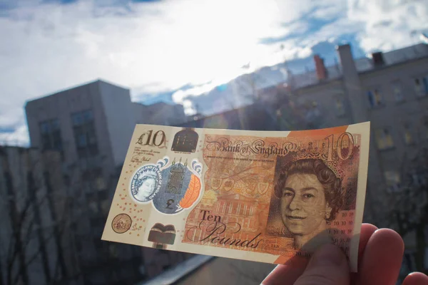 El, Queen ve Jane Austen 'in portresiyle polimer plastikten yapılmış yepyeni bir 10 sterlin tutuyor. Ve bankadaki şeffaf bir pencereden yansıyor.