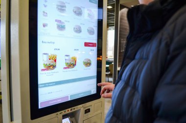 Moskova, Rusya, Kasım 2019: Bir adam hamburgerciyi bir self-servis terminali kullanarak seçiyor.