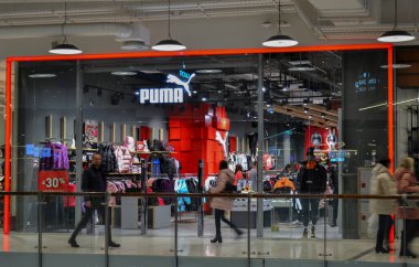 Moskova, Rusya, Kasım 2019: Marka spor giyim ve ayakkabı mağazası Puma. Alışveriş merkezindeki giriş, pencereler, mağazalar, alıcılar içerideki mallara bakıyor ve insanları bulanıklaştırıyor.