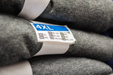 Üzerinde 2XL / / A boyunda 4XL yazan gri ve beyaz giysi yığını.