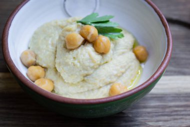 Tahta bir arka planda seramik kasede maydanoz ve nohut ile süslenmiş humus. 