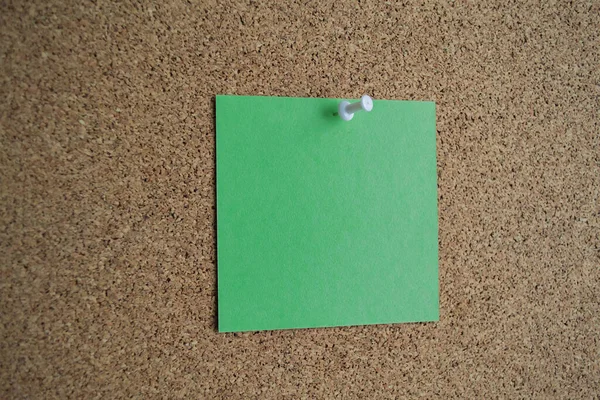 A green paper note on a cork Board, attached with a white pushpin. Copy space