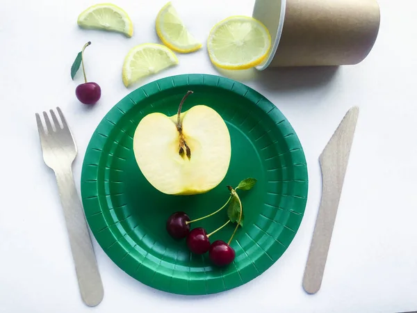 可生物降解餐具 带有柠檬楔子和樱桃的工艺杯 木制勺子和叉子 带有一半苹果的绿色纸盘和樱桃 回收和素食概念 — 图库照片