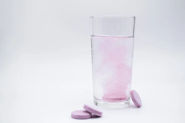 Su dolu bir bardakta, çözünebilir, hazır ya da erimiş pembe tablet baloncukları. Yakınlarda benzer haplar var: C vitamini, beslenme takviyeleri, ağrı kesiciler. Beyaz arkaplan, alanı kopyala