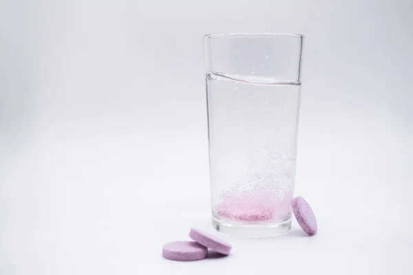 berrak bir bardakta, berrak suyla, çözünebilir bir bardakta. Anında veya pembe tablet baloncuklarını erit. Yakınlarda benzer haplar var: C vitamini, beslenme takviyeleri, ağrı kesiciler. Beyaz arkaplan, alanı kopyala