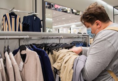 Moskova, Rusya, Temmuz 2020: Sakallı ve tıbbi maskeli genç bir adam elbise mağazasından pantolon seçiyor 