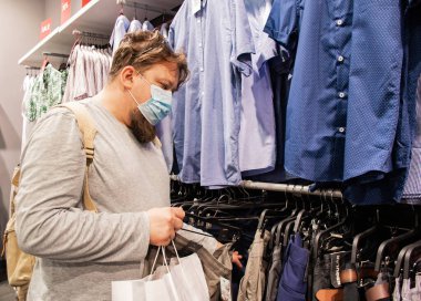 Moskova, Rusya, Temmuz 2020: Sakallı ve tıbbi maskeli genç bir adam bir giyim mağazasından gömlek ve pantolon seçiyor