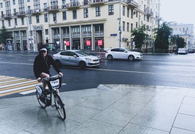 Moskova, Rusya, Temmuz 2020: Bisikletli bir bisikletçi, şehir merkezinde, Tverskaya Caddesi 'nde sağanak yağmur altında
