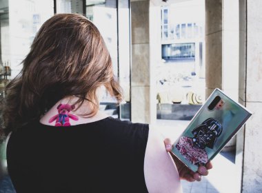 Moscow, Russia, July 2020: a View from the back of a girl with wind in her hair and a pink Teddy bear tattoo on her neck. She is holding a smartphone with a picture of Darth Vader in tattoos clipart