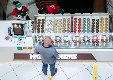 Moskova, Rusya, Temmuz 2020: Krispy Kreme çörek satış noktasının en iyi manzarası. Kel bir erkek müşteri, maskeli ve eldivenli satıcıların yiyeceklerini paketlemesini bekler..