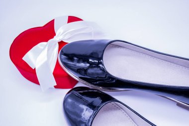 Kadınların siyah deri ayakkabıları. Bir tanesi beyaz kurdeleli kırmızı ipek bir kutuya basmış.