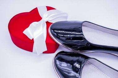 Kadınların siyah deri ayakkabıları. Bir tanesi beyaz kurdeleli, kalp şeklinde kırmızı bir ipek kutuya basmış..